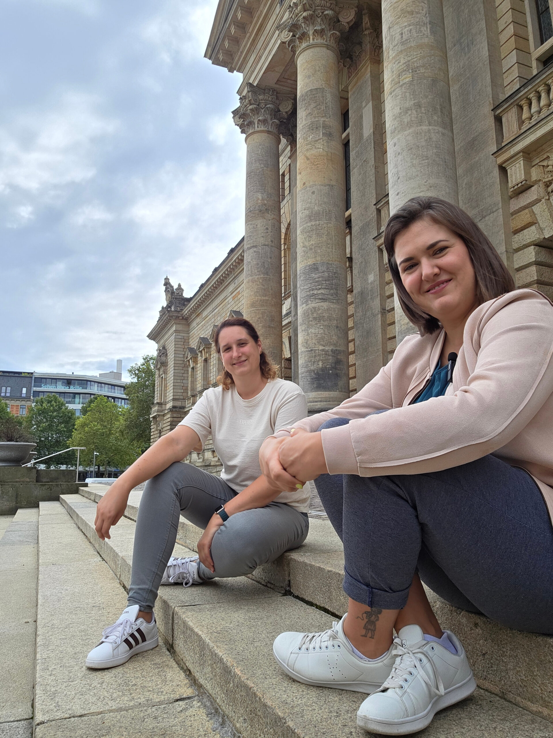 Die beiden Gründer sitzen auf Steinstufen vor einem Gebäude lächeln in die Kamera